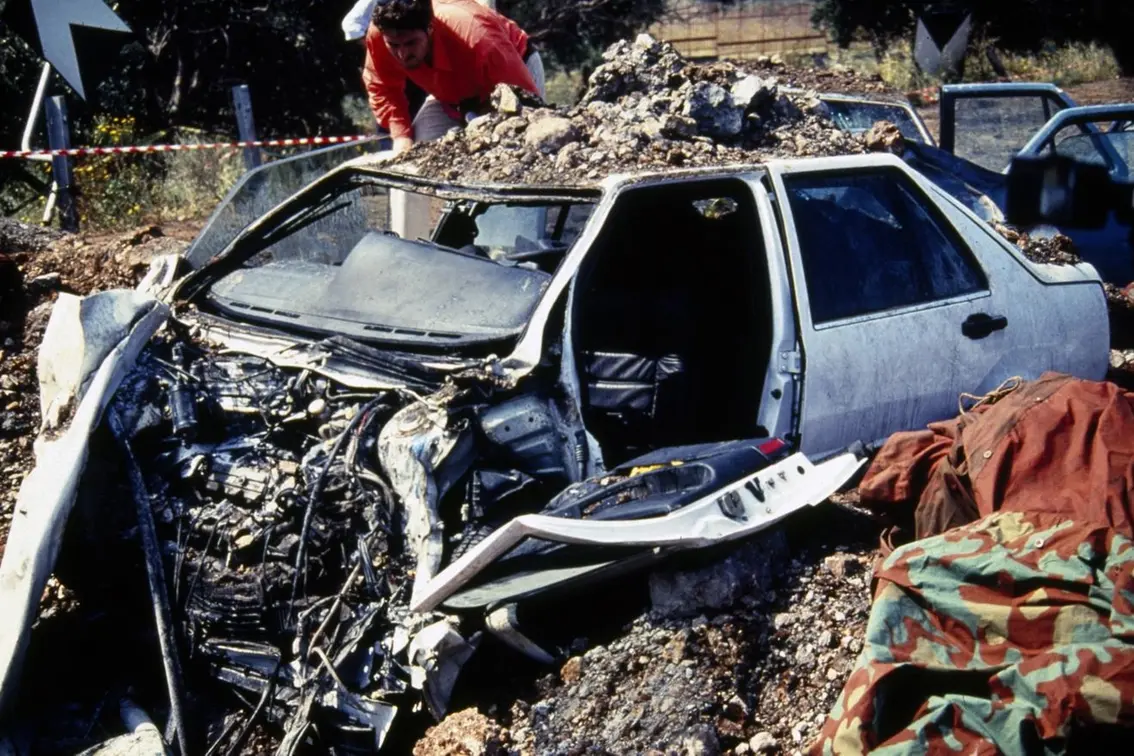 Nella foto, la voragine e i resti dell\\'auto su cui viaggiavano il giudice Giovanni Falcone, la moglie e gli uomini della scorta in seguito all\\'attentato che li ha colpiti e uccisi sull\\'autostrada per Palermo, all\\'altezza di Capaci