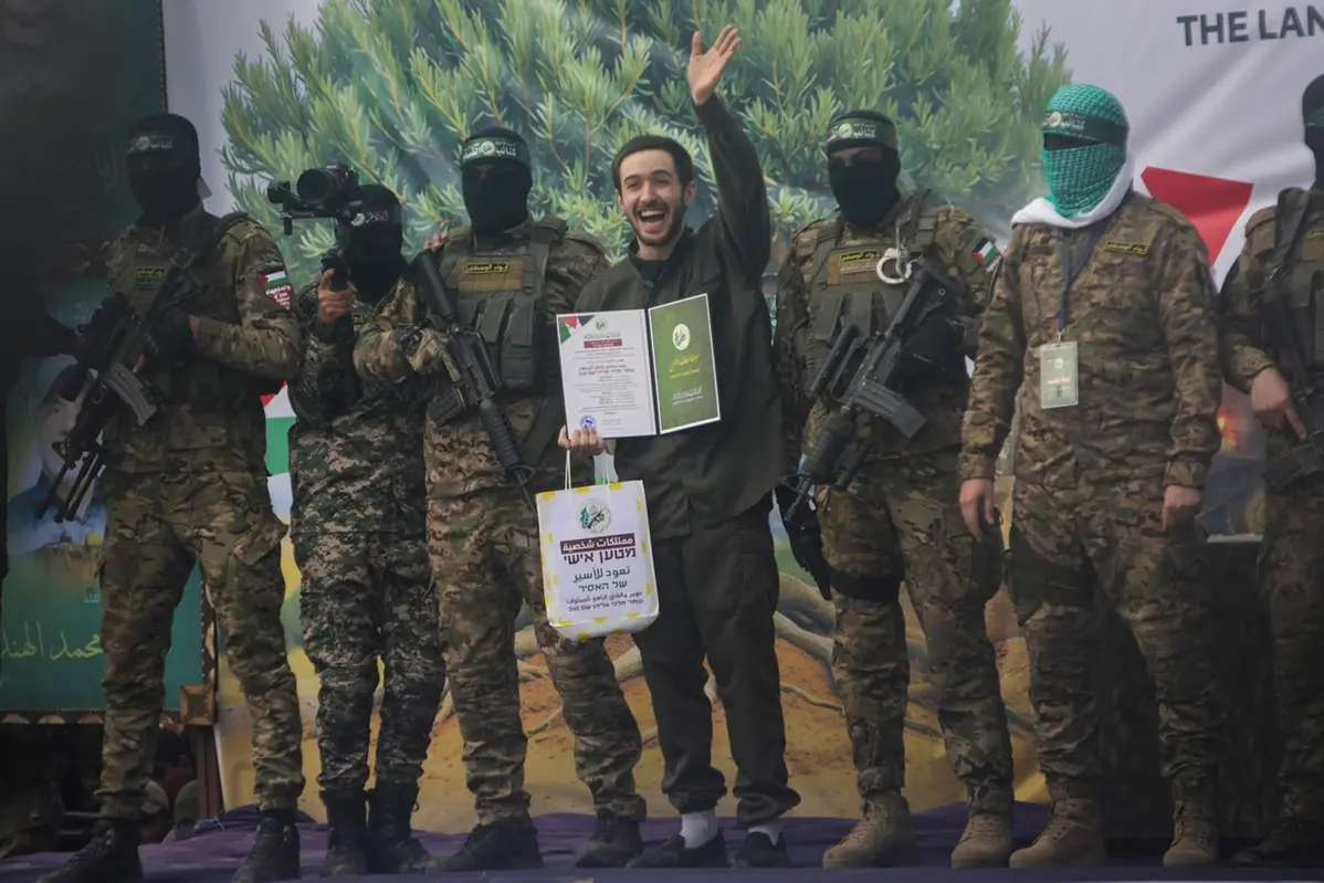 Israeli hostage Omer Shem, centre, waves as he shows, after being instructed by militants, a Hamas issued certificate, before being handed over to the Red Cross in Nuseirat, central Gaza Strip, Saturday, Feb. 22, 2025. (AP Photo/Jehad Alshrafi) , APN