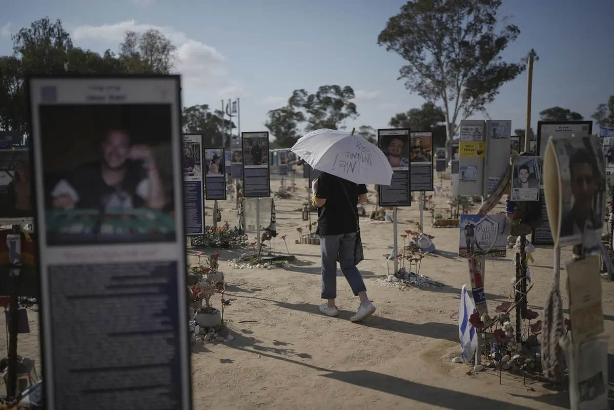 A woman walks with an umbrella reading \\'End the war immediately,\\' during a protest demanding immediate release of hostages held by Hamas in the Gaza Strip, at the site of the October 7, 2023, Hamas attack on the Nova music festival near Kibbutz Re\\'im in southern Israel, Wednesday, July 2, 2025. (AP Photo/Ohad Zwigenberg) , APN
