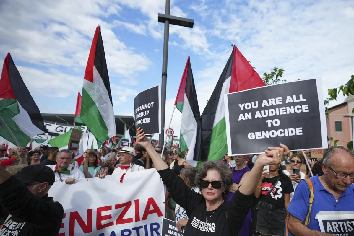 A demonstrator holds a placard that reads \\'You are all an audience to genocide\\' during a march in support of the Palestinian people in Gaza, during the Film Festival in Venice, Italy, Saturday, Aug. 30, 2025. (Photo by Alessandra Tarantino/Invision/AP) Associated Press/LaPresse , APN